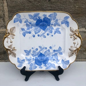 May include: A white square serving platter with a blue and gold floral design. The platter has a scalloped edge and gold trim.