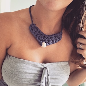 Peut inclure: Gros plan d'une femme portant un haut gris sans bretelles et un collier crocheté avec une perle en bois. Le collier est de couleur violet foncé.
