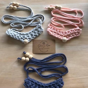 May include: Three crocheted necklaces with wooden beads. The necklaces are in gray, pink, and blue. The necklaces are handmade and have a simple design.