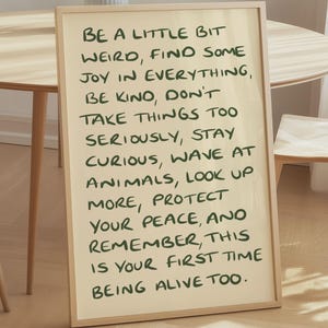 May include: A rectangular framed wall art piece with a light beige background and dark green handwritten text that reads: Be a little bit weird, find some joy in everything, be kind, don't take things too seriously, stay curious, wave at animals.