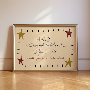 May include: A framed print with the handwritten text "How wonderful life is now you're in the world." The print has a gold frame and is decorated with green, red, and yellow stars.