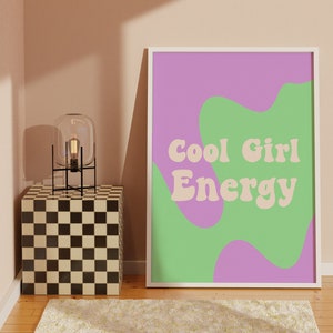 May include: A framed print with a white frame and a purple and green background. The text "Cool Girl Energy" is written in a retro font in a light peach colour.