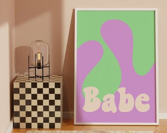 Puede incluir: Una impresión enmarcada con un diseño abstracto verde y morado y la palabra "Babe" en una fuente rosa claro.