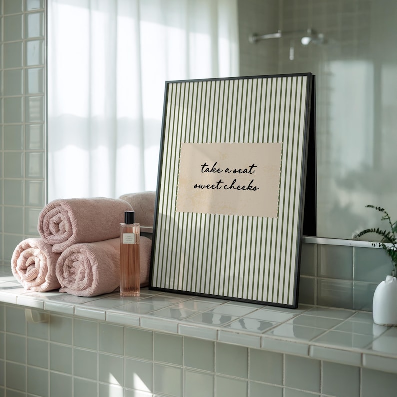 Funny bathroom wall art featuring olive green vertical pinstripes with a distressed cream scalloped label reading “take a seat sweet cheeks” in black handwritten script. Minimal vintage heritage inspired bathroom print with playful typography and a cosy boutique hotel aesthetic for guest bathrooms or powder rooms.