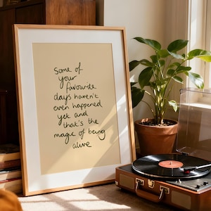 Minimalist typography print featuring the quote "Some of your favourite days haven't even happened yet and that's the magic of being alive" in an organic handwritten script. Warm beige background with olive green lettering creates a calming, hopeful and uplifting piece of inspirational wall art with a simple modern aesthetic.