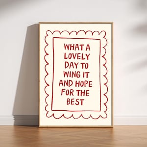 May include: A framed art print featuring the text "WHAT A LOVELY DAY TO WING IT AND HOPE FOR THE BEST" in red on an off-white background. The frame has a scalloped edge and a light wood finish.