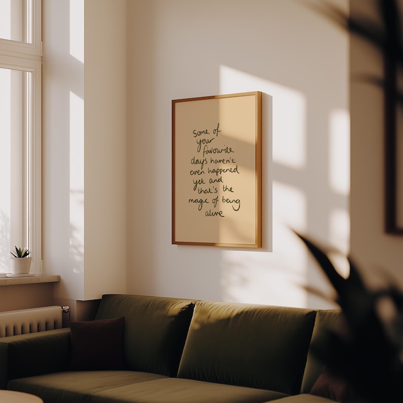 Minimalist typography print featuring the quote "Some of your favourite days haven't even happened yet and that's the magic of being alive" in an organic handwritten script. Warm beige background with olive green lettering creates a calming, hopeful and uplifting piece of inspirational wall art with a simple modern aesthetic.