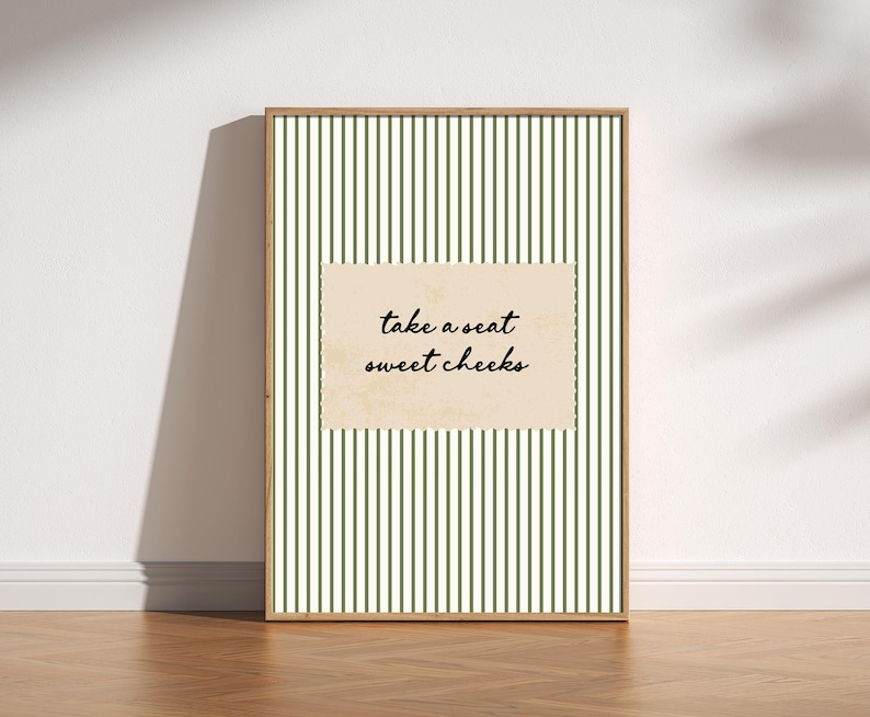 Funny bathroom wall art featuring olive green vertical pinstripes with a distressed cream scalloped label reading “take a seat sweet cheeks” in black handwritten script. Minimal vintage heritage inspired bathroom print with playful typography and a cosy boutique hotel aesthetic for guest bathrooms or powder rooms.