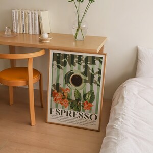 May include: A framed art print featuring a coffee cup and the word "ESPRESSO" in a vintage style. The print has a green and white striped background with orange flowers. The print is displayed on a wooden desk next to a chair and a bed.