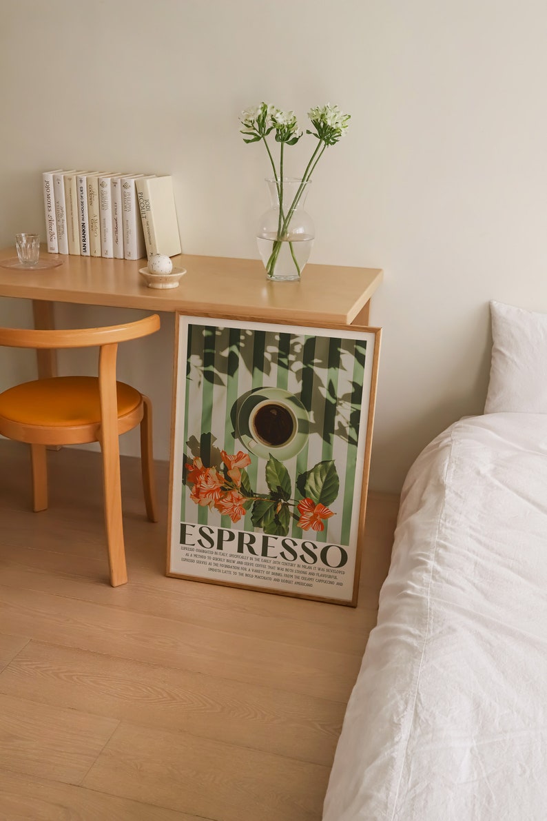 May include: A framed art print featuring a coffee cup and the word "ESPRESSO" in a vintage style. The print has a green and white striped background with orange flowers. The print is displayed on a wooden desk next to a chair and a bed.