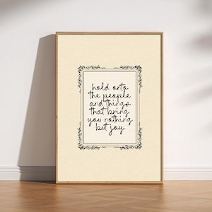 May include: A framed print with the text "hold onto the people and things that bring you nothing but joy." The text is in black script within a decorative black border on a cream-coloured background. The frame is a light brown colour.