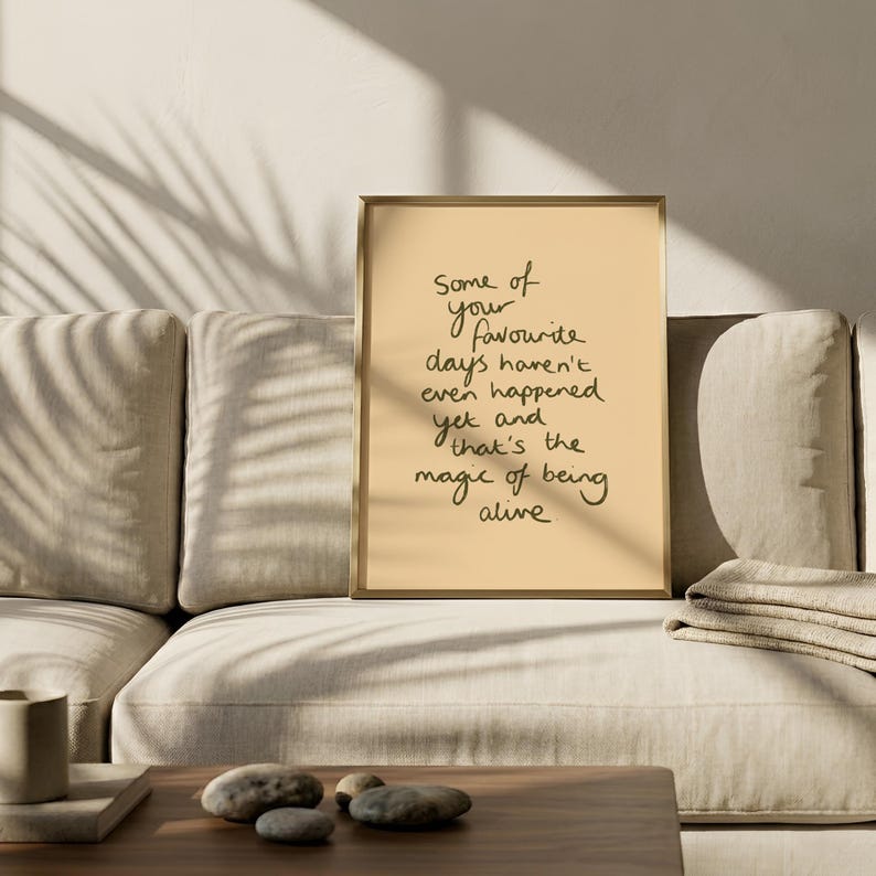 Minimalist typography print featuring the quote "Some of your favourite days haven't even happened yet and that's the magic of being alive" in an organic handwritten script. Warm beige background with olive green lettering creates a calming, hopeful and uplifting piece of inspirational wall art with a simple modern aesthetic.