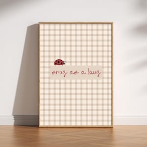 Peut inclure: Impression encadrée avec un fond à carreaux beiges et blancs. Un dessin de coccinelle rouge est au-dessus de la phrase "snug as a bug" en cursive rouge. Le cadre est de couleur marron clair.
