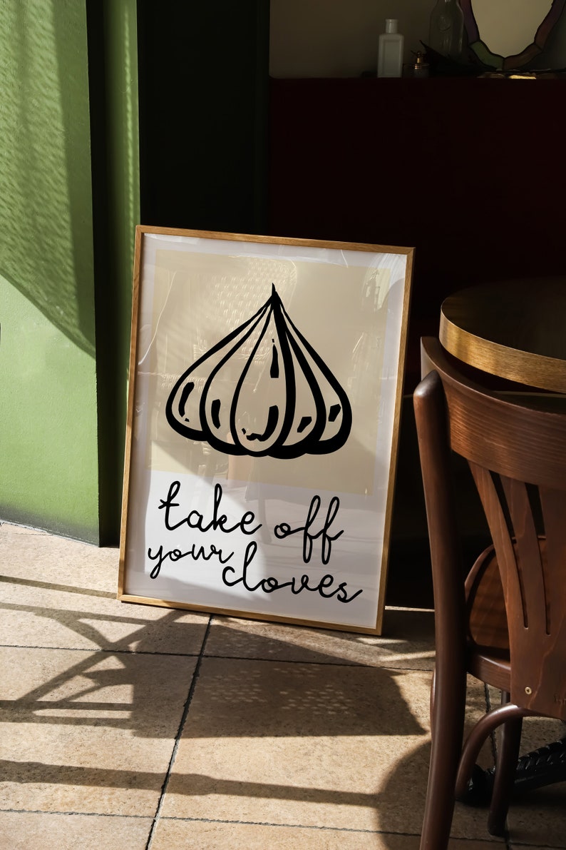 Op de afbeelding: Een ingelijst print met een zwart-witte illustratie van een teentje knoflook. De tekst "take off your cloves" staat onder de illustratie.
