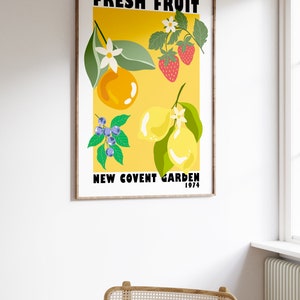 May include: A vintage poster with a yellow background featuring a stylized illustration of fresh fruit, including lemons, oranges, blueberries, and strawberries. The text "FRESH FRUIT NEW COVENT GARDEN 1974" is printed in black at the top and bottom of the poster.