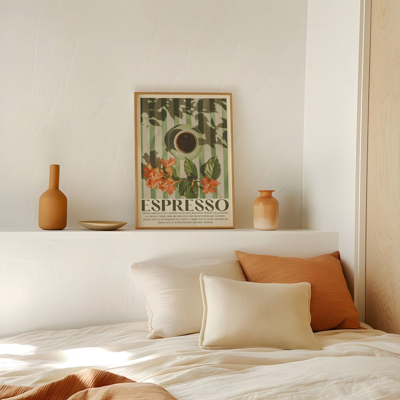 May include: A framed "Espresso" poster with a coffee cup illustration, orange flowers, and green stripes. The poster is displayed above a bed with cream-colored pillows and an orange throw. Two ceramic vases and a small plate are also visible.