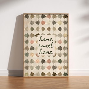 May include: Framed wall art featuring a star pattern in muted colors of pink, green, and brown. The words "home sweet home" are written in a cursive font on a cream-colored background. The artwork is displayed on a wooden floor.