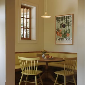 May include: A dining area with a round wooden table, two chairs, and a built-in bench. A framed poster with the word "ESPRESSO" hangs on the wall. A window with a wooden frame is visible. A light fixture hangs above the table.
