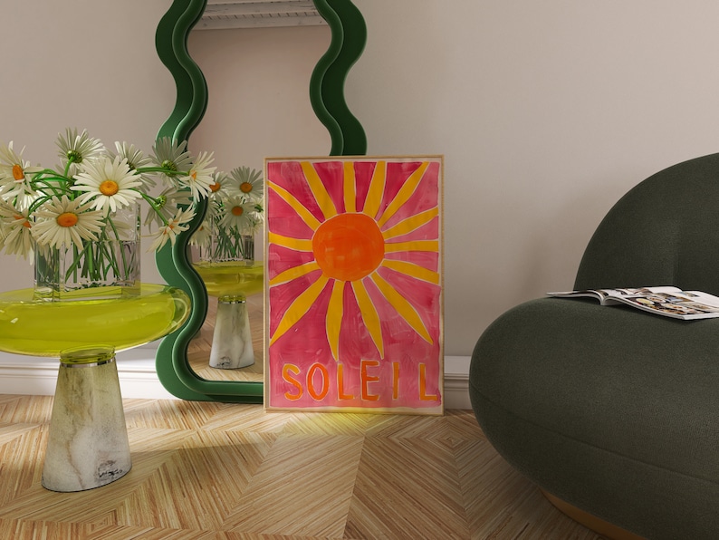 May include: A green wavy mirror with a pink and yellow sunburst print with the word "SOLEIL" at the bottom. The print is hanging on a wall next to a green armchair with a magazine on it.