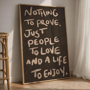May include: A rectangular framed wall art piece featuring a dark brown background with light beige hand-painted style lettering that reads: Nothing to prove, just people to love and a life to enjoy. The frame is made of light-coloured wood.