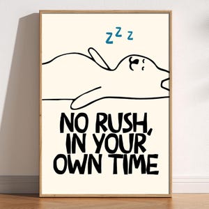 May include: A framed art print with a cream background. The print features a sleeping cartoon figure with the text "No rush, in your own time" in black, and blue "z"s above the figure. The artwork is in a wooden frame.