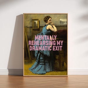 Puede incluir: Una impresión artística enmarcada que presenta una pintura vintage de una mujer con un vestido azul. El texto rosa "MENTALLY REHEARSING MY DRAMATIC EXIT" está superpuesto. La obra de arte se exhibe sobre un suelo de madera.