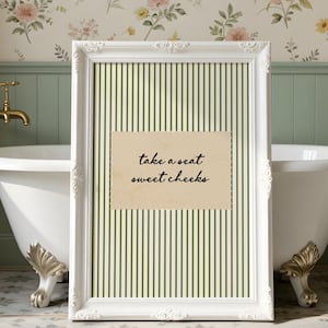 Funny bathroom wall art featuring olive green vertical pinstripes with a distressed cream scalloped label reading “take a seat sweet cheeks” in black handwritten script. Minimal vintage heritage inspired bathroom print with playful typography and a cosy boutique hotel aesthetic for guest bathrooms or powder rooms.