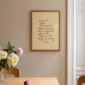 Minimalist typography print featuring the quote "Some of your favourite days haven't even happened yet and that's the magic of being alive" in an organic handwritten script. Warm beige background with olive green lettering creates a calming, hopeful and uplifting piece of inspirational wall art with a simple modern aesthetic.