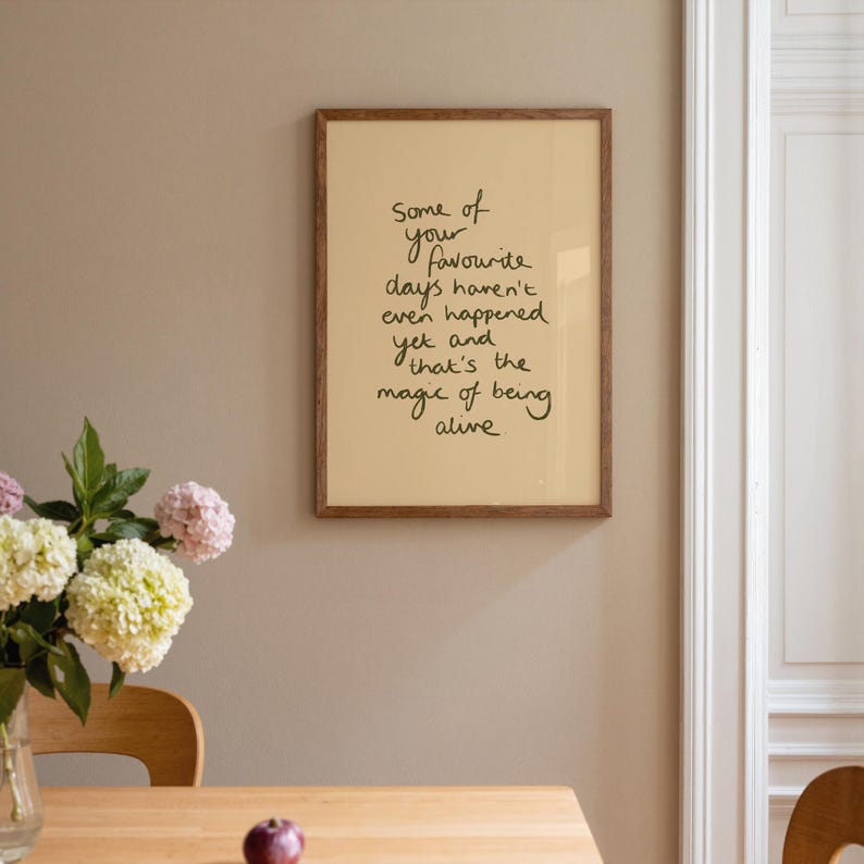 Minimalist typography print featuring the quote "Some of your favourite days haven't even happened yet and that's the magic of being alive" in an organic handwritten script. Warm beige background with olive green lettering creates a calming, hopeful and uplifting piece of inspirational wall art with a simple modern aesthetic.