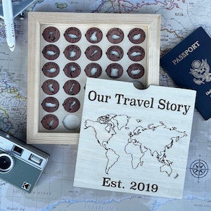 May include: A light-coloured wooden box with a sliding lid featuring the text Our Travel Story and Est. 2019 above a world map outline. Inside are circular wooden tokens with country names and map shapes, including Italy, Jamaica, Canada, and others.