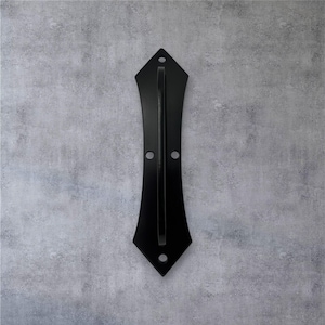 May include: A black metal door pull with a decorative design. The pull is approximately 12 inches long and features a handle and mounting holes. The design is symmetrical and has a pointed top and bottom.