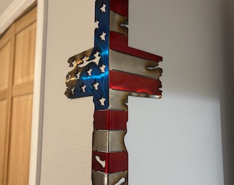 May include: A metal cross with a distressed American flag design. The cross is mounted on a wall and is made of metal.