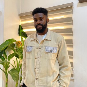 Peut inclure: Une veste en jean beige avec un détail de poche à carreaux bleu clair et blanc. La veste a une fermeture à boutons et des manches longues.