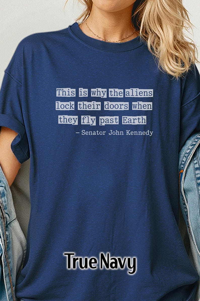 Op de afbeelding: Marineblauw T-shirt met de quote "Daarom sluiten de aliens hun deuren als ze langs de aarde vliegen - Senator John Kennedy" in witte tekst. Het shirt heeft een ronde hals.