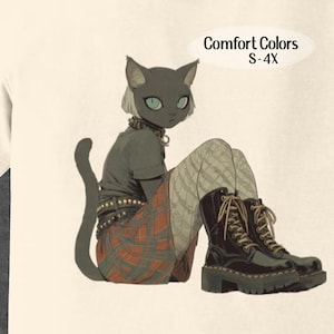 May include: Cream-colored t-shirt featuring a stylized illustration of a cat-like figure in a punk aesthetic. The figure wears a studded collar, plaid skirt, and black boots. The text "Comfort Colors S-4X" is in an oval shape.
