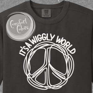 May include: Dark gray sweatshirt with the text "It's a Wiggly World" and a white peace sign design. The sweatshirt also features the Comfort Colors logo on the upper left.