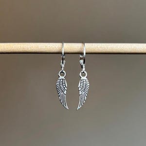 Pode incluir: Um par de brincos de prata com forma de asas de anjo com um design de aro.