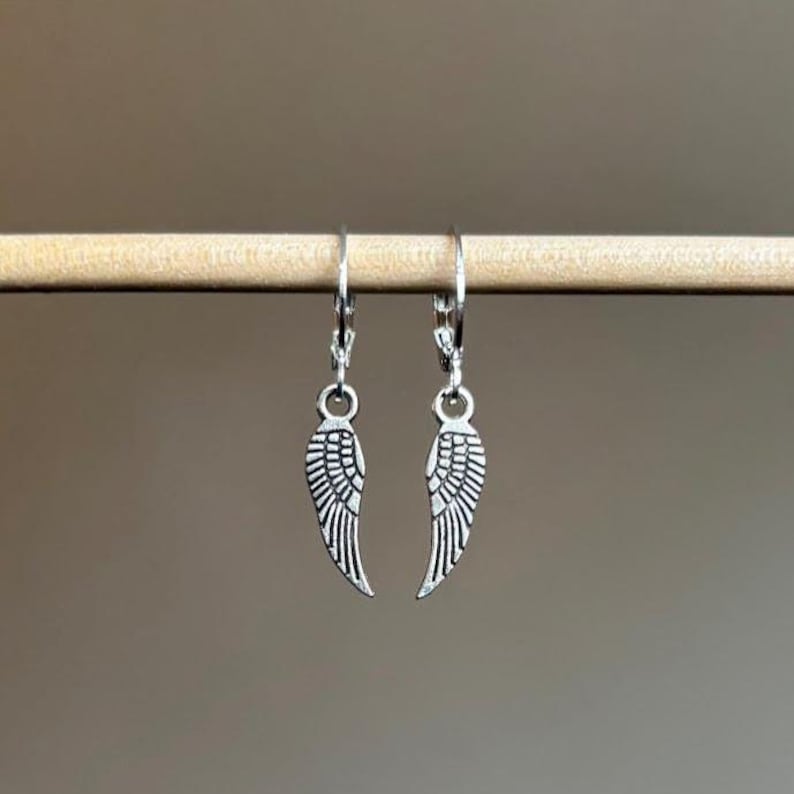 Pode incluir: Um par de brincos de prata com forma de asas de anjo com um design de aro.