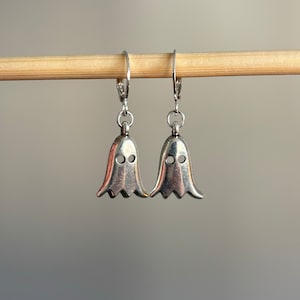May include: A pair of silver ghost-shaped dangle earrings with a hook closure.