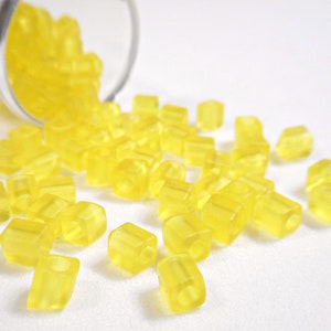 May include: A close-up of a pile of small, translucent yellow beads. The beads are square-shaped and have a slightly frosted finish.
