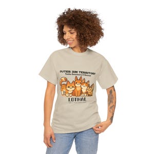 Op de afbeelding: Een lichtbeige t-shirt met een cartoonillustratie van vijf oranje en witte katten. De tekst "OUTER RIM TERRITORY Tooka Sanctuary & Rescue" en "LOTHAL" zijn boven en onder de kattenafbeelding gedrukt.