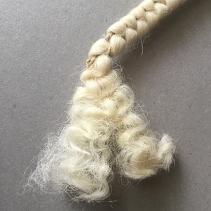 May include: Close-up of a cream-colored, braided rope with a frayed end. The rope is made of natural fibers and has a textured appearance. The background is a solid gray surface.