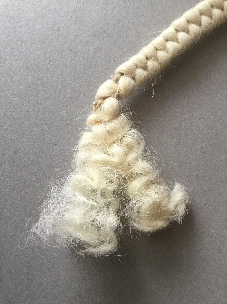 May include: Close-up of a cream-colored, braided rope with a frayed end. The rope is made of natural fibers and has a textured appearance. The background is a solid gray surface.