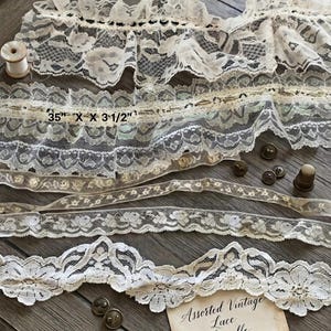 May include: An assorted bundle of cream-colored lace trims featuring various floral and geometric patterns, a small wooden spool of white thread, four metal buttons, a metal thimble, and a card labeled Assorted Vintage Lace Bundle, 35" x 3 1/2".