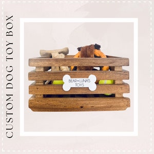 May include: A wooden crate with a white bone-shaped label that says "Bear + Luna's Toys". The crate is filled with dog toys, including a rope toy, a bone, and tennis balls.