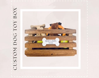 May include: A wooden crate with a white bone-shaped label that says "Bear + Luna's Toys". The crate is filled with dog toys, including a rope toy, a bone, and tennis balls.