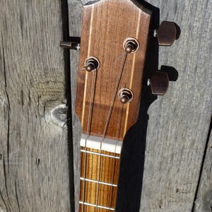 May include: Close-up of the headstock of an acoustic guitar. The headstock is made of wood and has a light brown finish. There are six tuning pegs on the headstock, and the strings are attached to the tuning pegs. The strings are made of metal and are silver in colour.