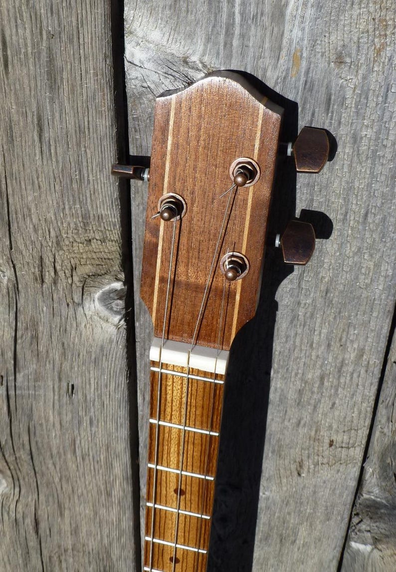 May include: Close-up of the headstock of an acoustic guitar. The headstock is made of wood and has a light brown finish. There are six tuning pegs on the headstock, and the strings are attached to the tuning pegs. The strings are made of metal and are silver in colour.