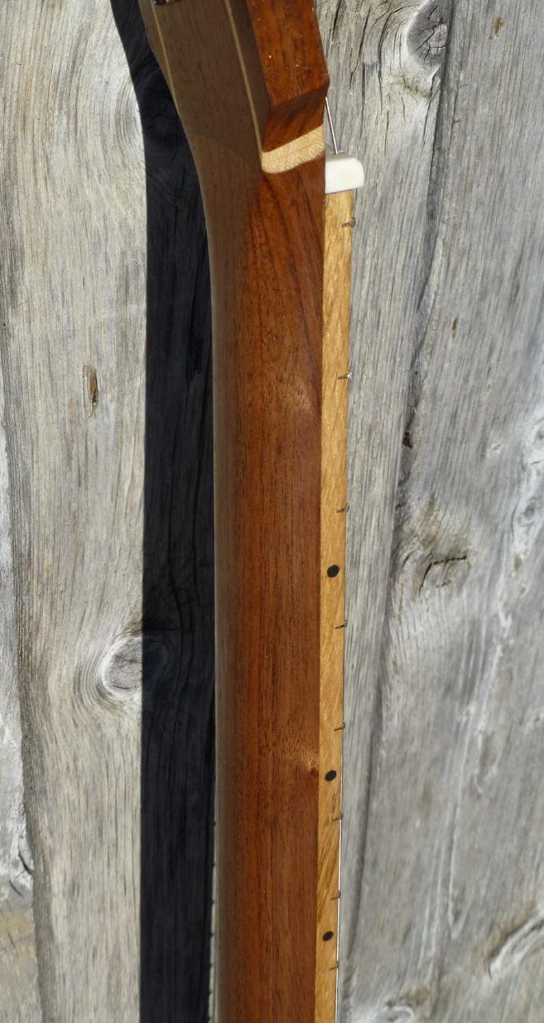 May include: Close-up of the back of a guitar neck. The neck is made of dark wood with a light wood inlay down the centre. The neck has a white nut and black dots as position markers.