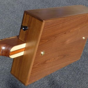 May include: A wooden box with a guitar neck attached to the side. The box is made of dark wood with a light wood trim. The guitar neck is made of light wood with a dark wood fretboard.